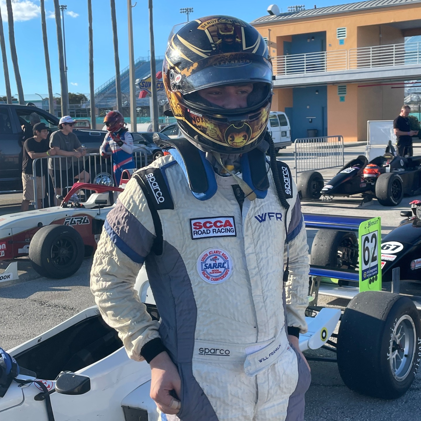 Will in his custom helmet and racing suit beside the white race car.